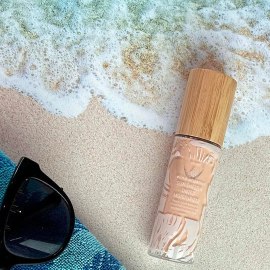 Elina Organics Sun Shelter Tinted Moisturizer on a sandy beach near the water.