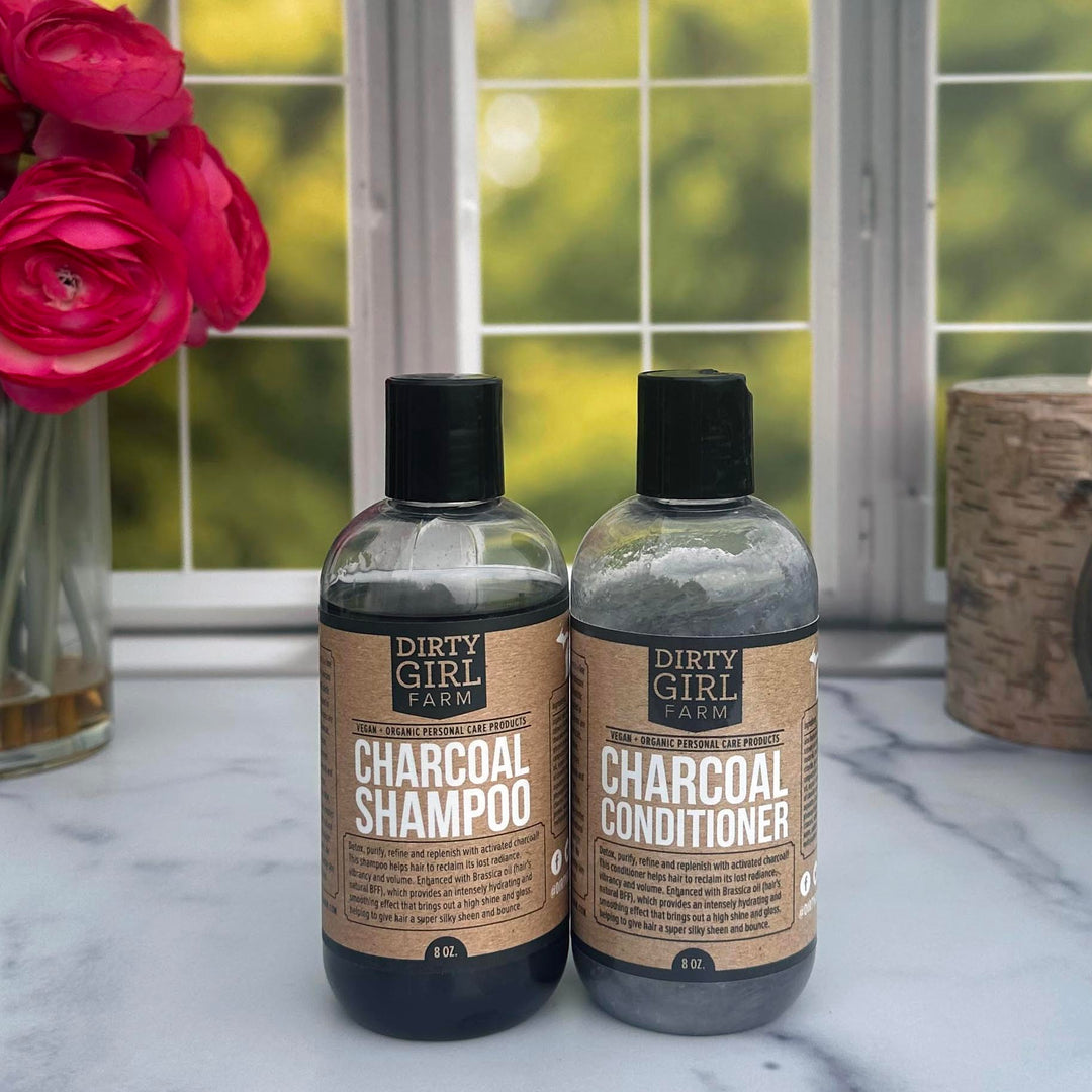 Dirty Girl Farm Charcoal Shampoo and Conditioner in front of a window with flowers and a wood like candle