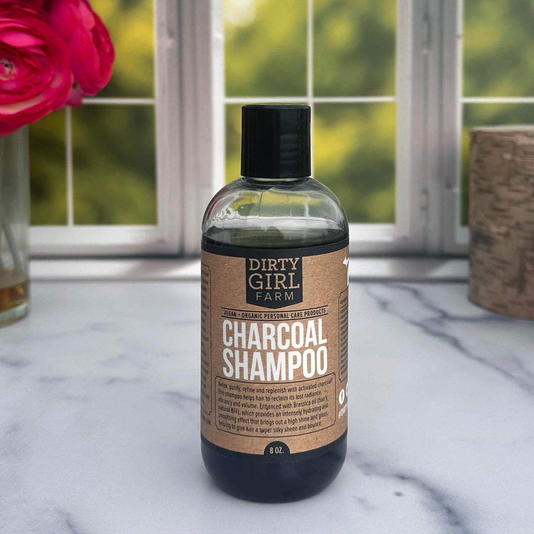 Dirty Girl Farm Charcoal Shampoo in front of a window with a vase of flowers and a candle.