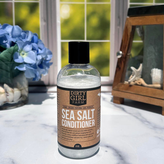 Dirty Girl Farm Sea Salt Conditioner in front of a window with a vase of flowers off to the side.