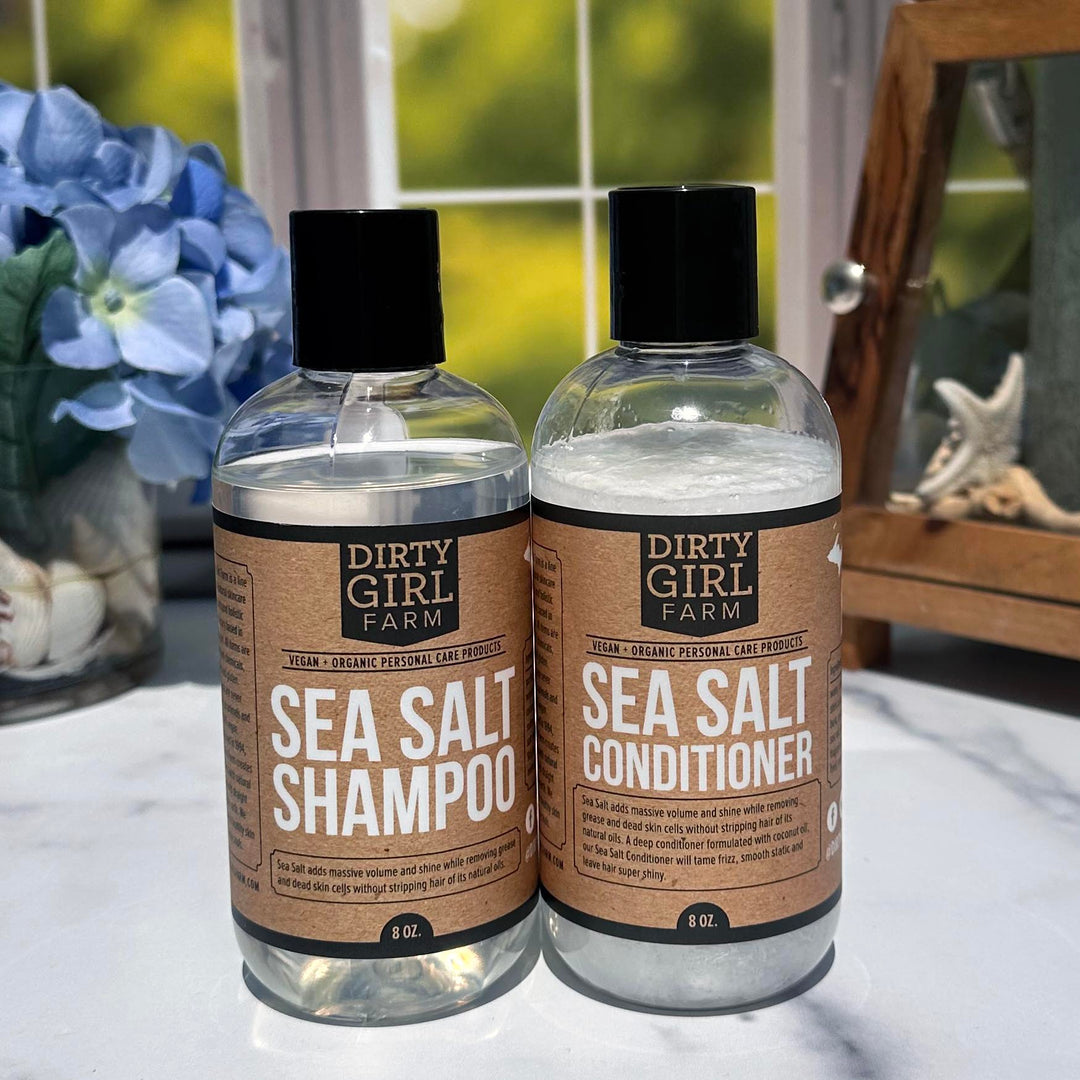 Dirty Girl Farm Sea Salt Shampoo and Conditioner in front of a window and a vase of flowers.